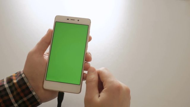 Man using smartphone with green screen . Smart phone charging with USB charger close-up connection in hands - USB data cable connecting on modern gadget. Chroma key. Green screen.