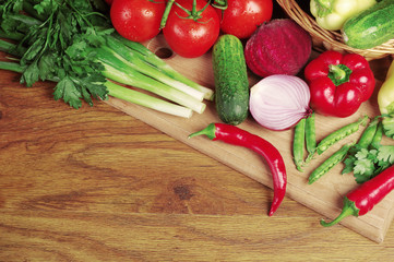 Appetizing vegetables on a wooden table. Tomatoes, cucumbers, onions, carrots, peppers, parsley.