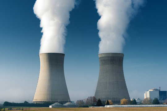 two power plant cooling towers steaming on dark blue sky background