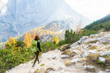 Young woman wearing backpack is hiking in the mountains among the yellow larches in Julian Alps, Slovenia. Adventure and hiking concept.