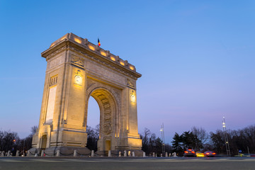 Fototapeta na wymiar Low angle of Arch of Triumph (Arcul de Triumf) in Bucharest, Romania, at sunset / blue hour. With a height of 27 metres, this arch was inaugurated on 1 December 1936 and it's made of stone.