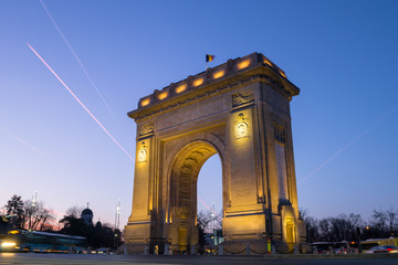 Fototapeta na wymiar Arch of Triumph (Arcul de Triumf) in Bucharest, Romania, at sunset, with blue and pink skies. Low angle and long exposure shot of this triumphal monument located on Kiseleff Road.