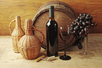 A glass of wine, a bottle, grapes on the background of a wine barrel.
