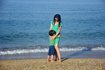 Fototapeta na wymiar Mother and son playing on the beach. Mom and child hugging and enjoy by the sea