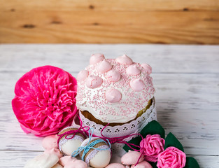 Easter cake and eggs with paper flowers on a wooden table against the background of a wooden wall.