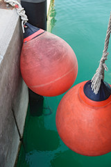 Two hanging red plastic fender are near concrete mooring wall.