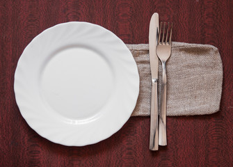 Empty plate on colorful tablecloth with fork and knife above wooden table