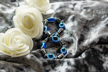 Blue bracelet made of natural stones for women's day, March 8. Figure in the form of eyes and pupil from evil eye, anger and detractors. On grey velvet with white roses.