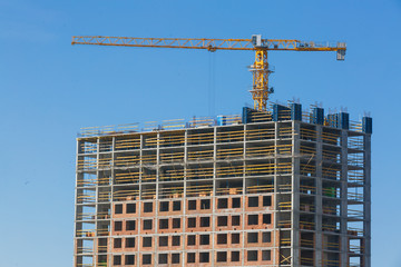 Fototapeta na wymiar Crane and building under construction against blue sky