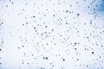 Dirty window glass with drops of rain. Atmospheric blue light background with raindrops. Droplets and stains close up. Detailed transparent texture in macro with copy space. Rainy weather.