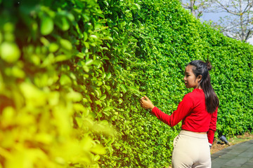 Beautiful Asian woman in red top standing aside the green plant wall
