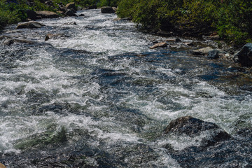 Natural texture of foamed water surface. Rapids of river close-up. Fast flow in mountain creek. Background of clean water waves with copy space. Textured foam of shiny stream. Fast river texture.