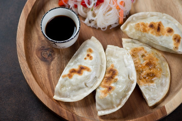 Close-up of pan fried korean potstickers on a round wooden serving tray, high angle view