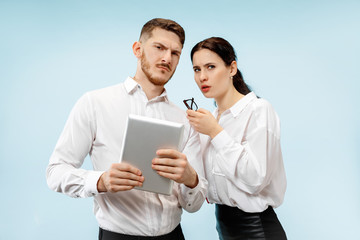 Concept of partnership in business. Young man and woman looking suspicious against blue background at studio