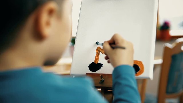 Child paints a bicycle on canvas. Over shoulder view of childish painting in focus.
