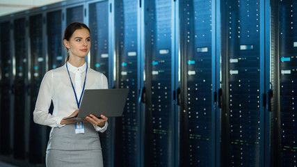 Beautiful Data Center Female IT Technician Walking Through Server Rack Corridor with a Laptop...