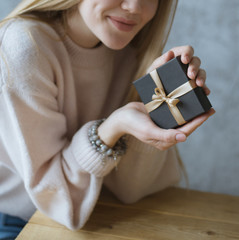 girl holds a small black gift box tied with a ribbon, woman holds a small black gift box tied with a ribbon.