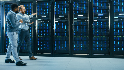 IT Technician with a Laptop Computer and Black Male Engineer Colleague are Talking in Data Center...