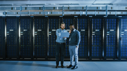 Bearded IT Technician in Glasses with a Laptop Computer and Black Male Engineer Colleague Have...
