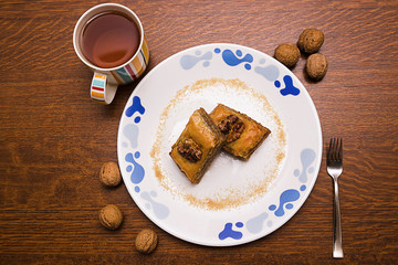 Baklava on a white plate, cup with tea, fork, walnuts