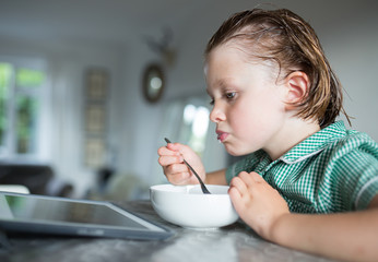 female child eating breakfast at the table in her school uniform watching the iPad 