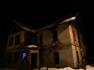 Fototapeta na wymiar Old, creepy , abandoned crumbling house at night near a parking lot at wintertime.