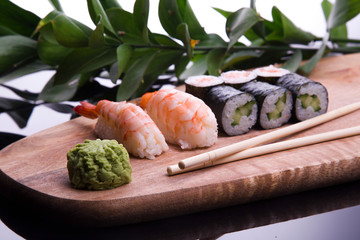 set of sushi on a wooden board with leaves of plants on a dark background