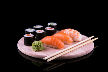 set of sushi on a wooden board with leaves of plants on a dark background