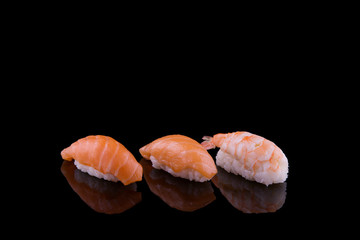 set of sushi on a wooden board with leaves of plants on a dark background