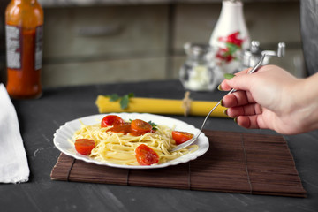 Spaghetti pasta in tomato sauce with cheese and parsley, woman's hand. Italian spaghetti pasta over dark stone background.