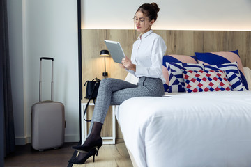 Attractive young businesswoman using her digital tablet sitting on the bed at hotel room.
