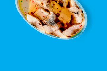 One oval transparent plastic container of canned seafood and spice in marinade on blue table on cuisine with copy space for your text. Top view. Breakfast concept