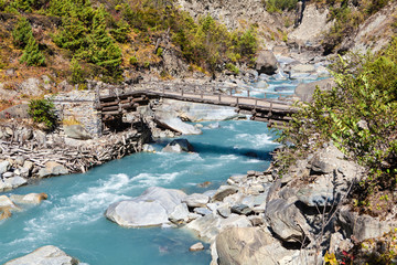 Wooden bridge across a turquoise fast river in Himalayas mountains