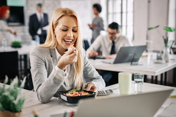 Happy businesswoman eating vegetable salad on lunch break.