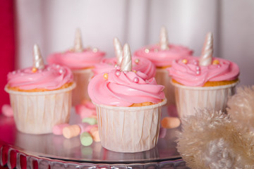 First baby girl birthday party concept. Candy bar with sweet unicorn cakes and decor items in bright pink colors.