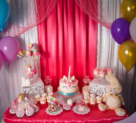 Sweet table and big unicorn cake for baby girl first birthday. Candy bar with a lot of different candies and sweet cakes