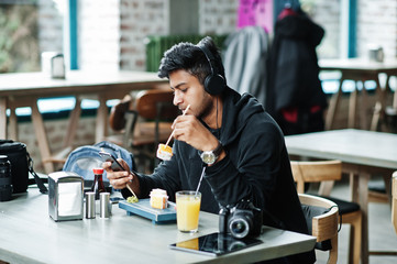 Casual and stylish young asian man with earphones at cafe eating sushi.