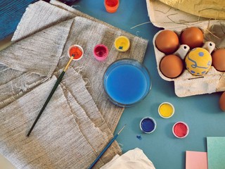Eggs, colorful paints, brushes, pencils on a blue background, top view, coloring eggs, preparing for Easter, spring seasonal holiday