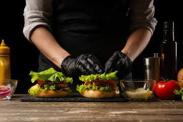 The chef lays out a fresh salad on a burger, with ingredients in the background. Horizontal photo, Tasty and unhealthy food, fast food, homemade recipes, restaurant, catering, recipe book