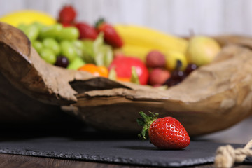 Erdbeere liegt vor einer Schüssel mit Obst