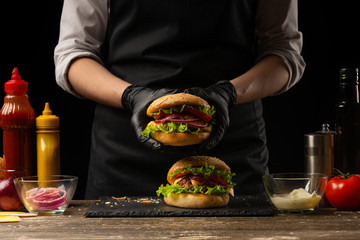 the chef prepares a burger, a hamburger. on a background with ingredients. Delicious and fast food, fast food. A menu, a cafe, fast food, catering, gastronomy - obrazy, fototapety, plakaty