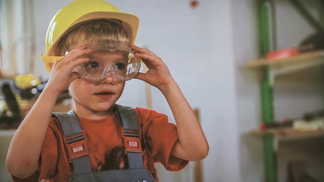 Child with protection helmet and glasses. Portrait shot of kid in focus putting on helmet and glasses before working.