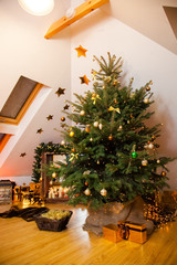 Christmas decorations in the studio, big natural fir tree with golden balls, bows and snowflakes, wooden fireplace and candles on it and brown cozy armchair