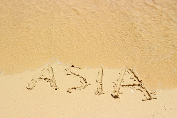 Sea wave erases the inscription Asia on the wet sand on the tropical beach.