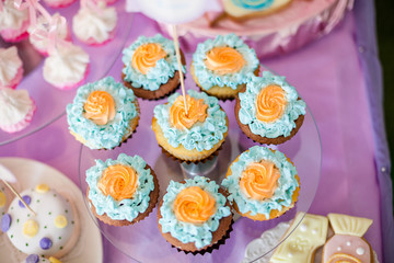 Birthday party concept. Table for kids with cupcakes with blue and orange top and decor items in bright pink and blue colors