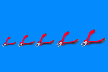 Row of nippers for wire with red and black handles from small to large on blue background