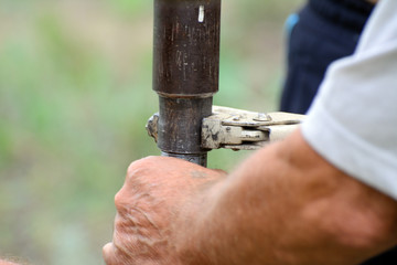 Male hands hold adjustable wrench wrapping the pipe.