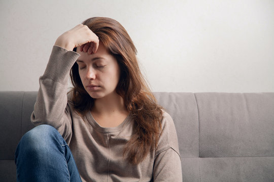 Frustrated girl sitting on the couch with a headache.