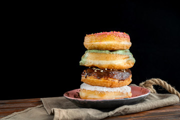 A stack of 4 donuts on a wooden tray and a black background.