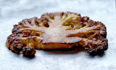 A large slice of roasted cauliflower on a silver background